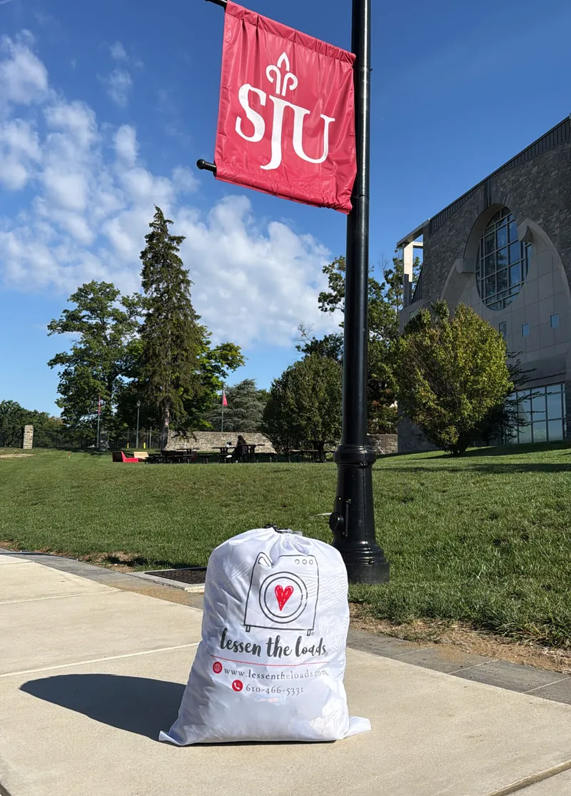 A Lessen the Loads laundry bag waiting on the sidewalk beneath a Saint Joseph's University banner