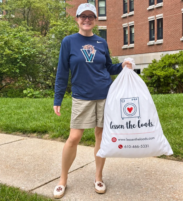 A Lessen the Loads specialist carrying a full branded laundry bag on the sidewalk outside a campus residence hall