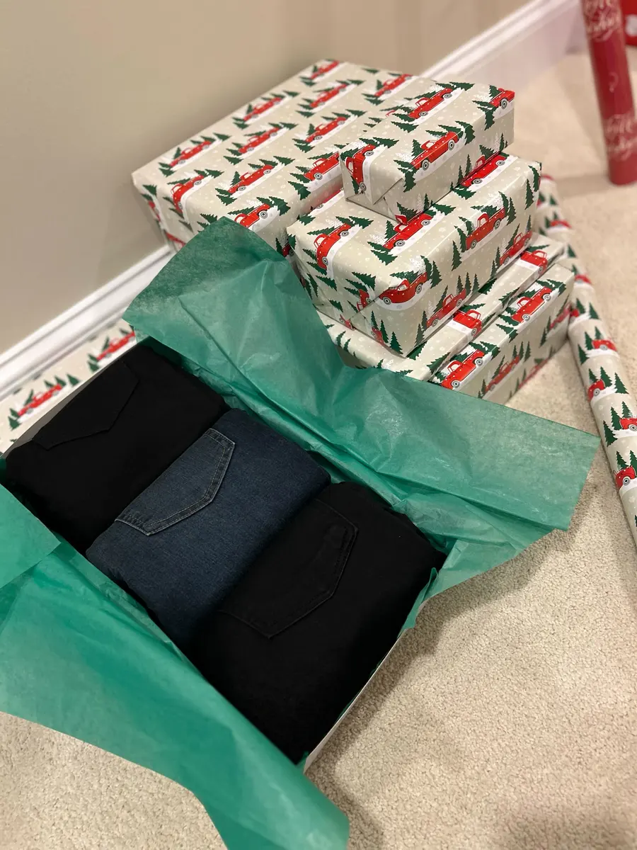 A gift box of folded clothes nested in green tissue paper, beside wrapped presents