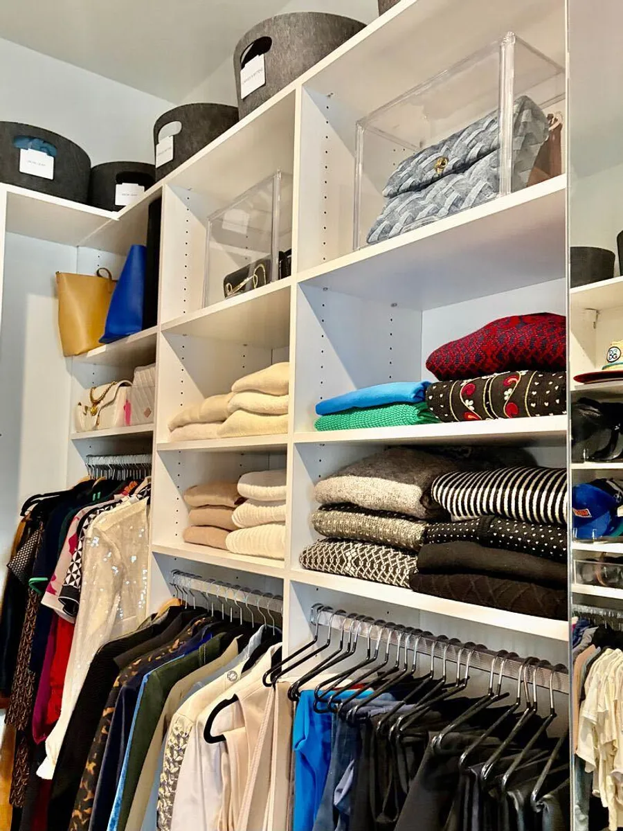 Folded sweaters and handbags in clear boxes on closet shelves