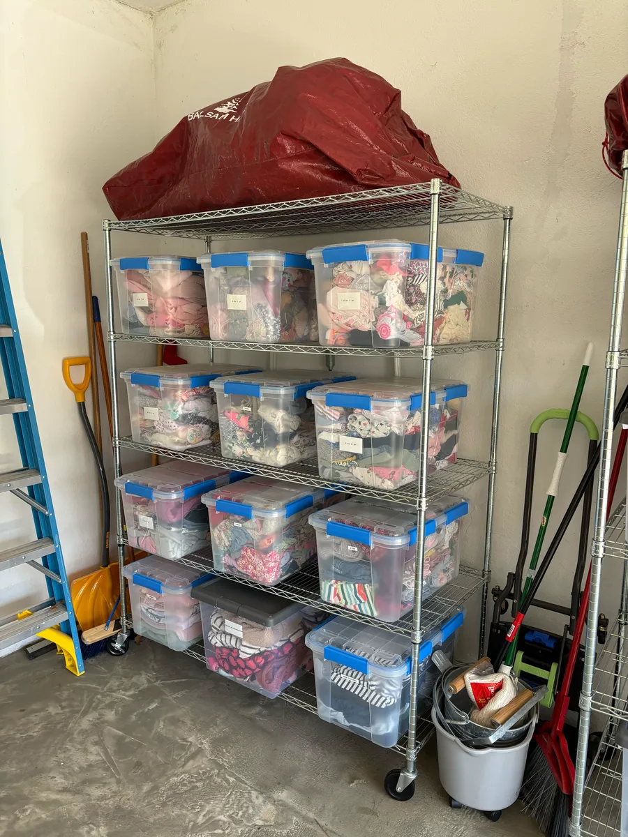 Kids' clothes in clear bins labeled by size on garage shelving