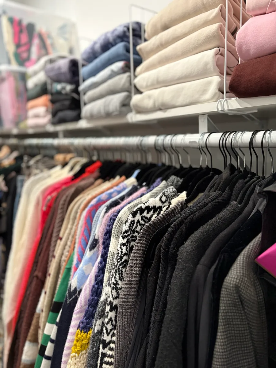 Sweaters hung by color below folded stacks on a closet shelf