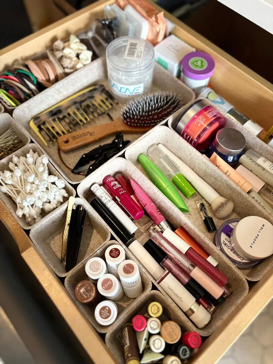 A vanity drawer of makeup and hair accessories sorted into trays