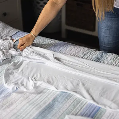 A team member folding a shirt on a residential bed