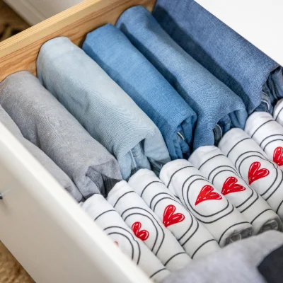 Neatly folded jeans and Lessen the Loads shirts in a drawer with the logo showing